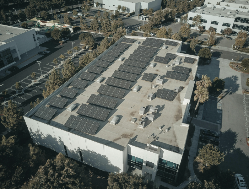 一座大型白色商業建築屋頂上安裝了多排太陽能板,周圍是停車場和樹木