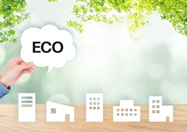 手持「ECO」字樣氣泡對話框/綠色植物背景下的白色剪紙房屋/生態友善和綠色城市規劃概念圖/環保建築與永續生活